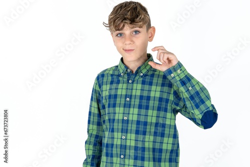 Displeased caucasian kid boy wearing plaid shirt shapes little hand sign demonstrates something not very big. Body language concept.