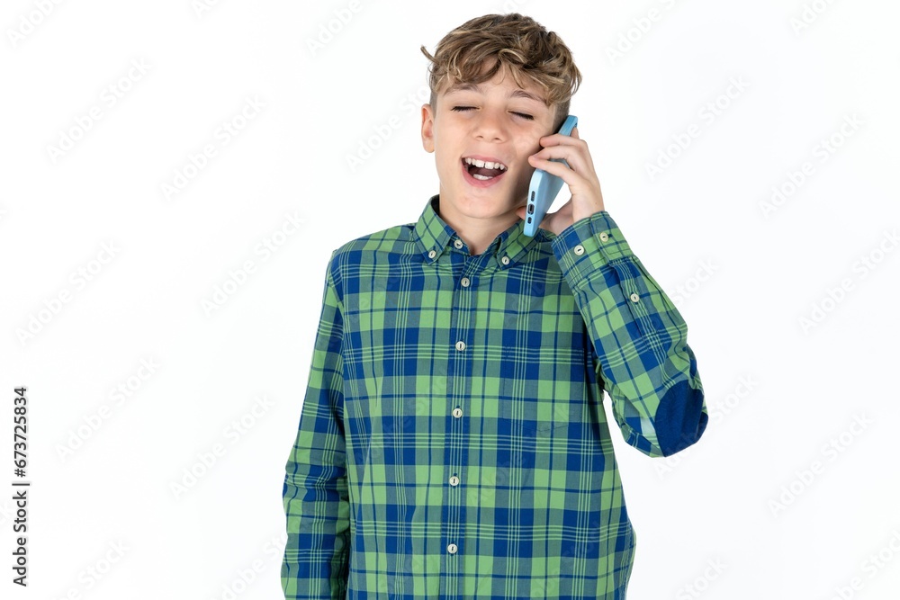 Overemotive happy caucasian kid boy wearing plaid shirt laughs out positively hears funny story from friend during telephone conversation Overemotive happy caucasian kid boy wearing plaid shirt laughs out positively hears funny story from friend during telephone conversation
