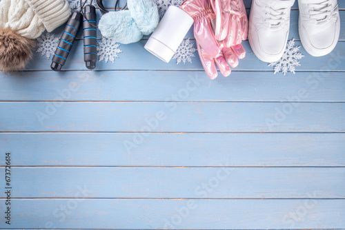 Fototapeta Naklejka Na Ścianę i Meble -  Winter sport and fitness, active lifestyle background. Warm knitted hat, sweater, jump rope, ski mask, thermal mug with hot tea, gloves, winter sneakers on wooden blue background, snowflakes, top view