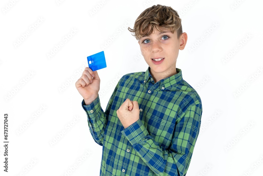 Excited happy positive cheerful smiling caucasian kid boy wearing plaid shirt hold credit card raise fist in victory Excited happy positive cheerful smiling caucasian kid boy wearing plaid shirt hold credit card raise fist in victory