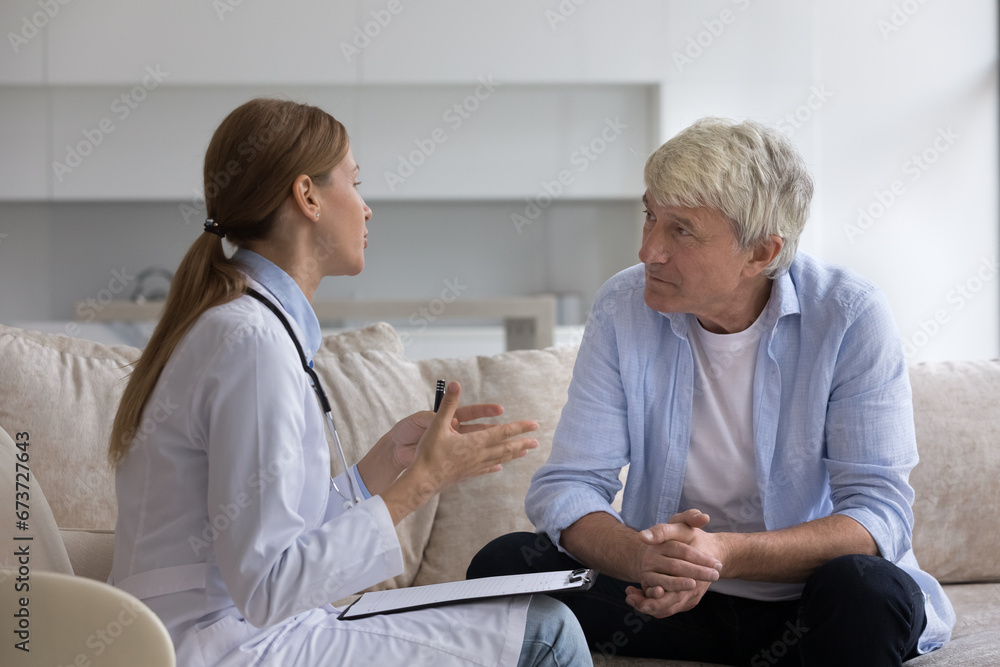 Fototapeta premium Cheerful senior patient meeting with doctor at home, talking to practitioner, smiling, laughing. Physician woman visiting older man for examination, consultation, giving therapy recommendation