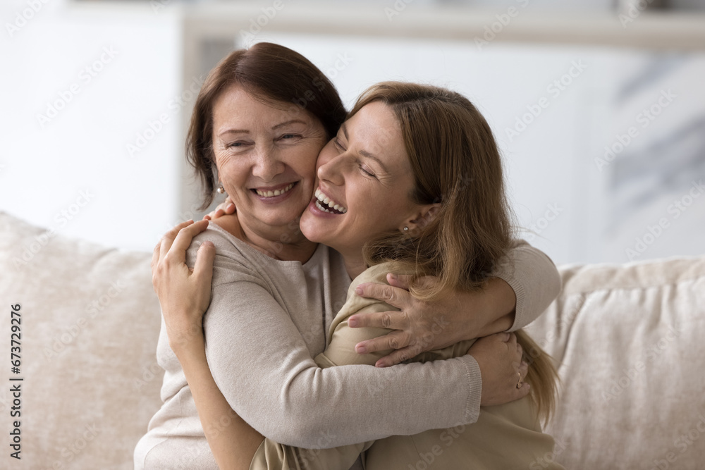 Happy loving elder mom embracing beautiful adult daughter woman with joy, tenderness, smiling, laughing at joke together, giving comfort, support, care, enjoying being parent, motherhood - obrazy, fototapety, plakaty 