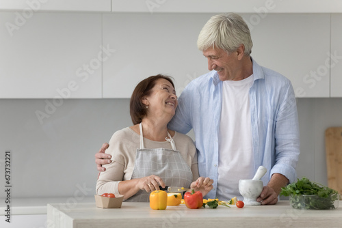 Positive excited adult daughter and senior father dancing in kitchen, having fun while cooking family dinner for party at home, laughing at table with ingredients, making pepper glasses, laughing © fizkes