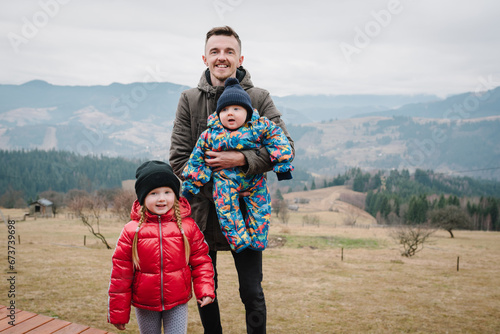 Dad, daughter, hug son enjoy time together. Active weekend travel concept in mountains. Father embraces baby and kids on a terrace on an autumn day. People stand in backyard of country house.