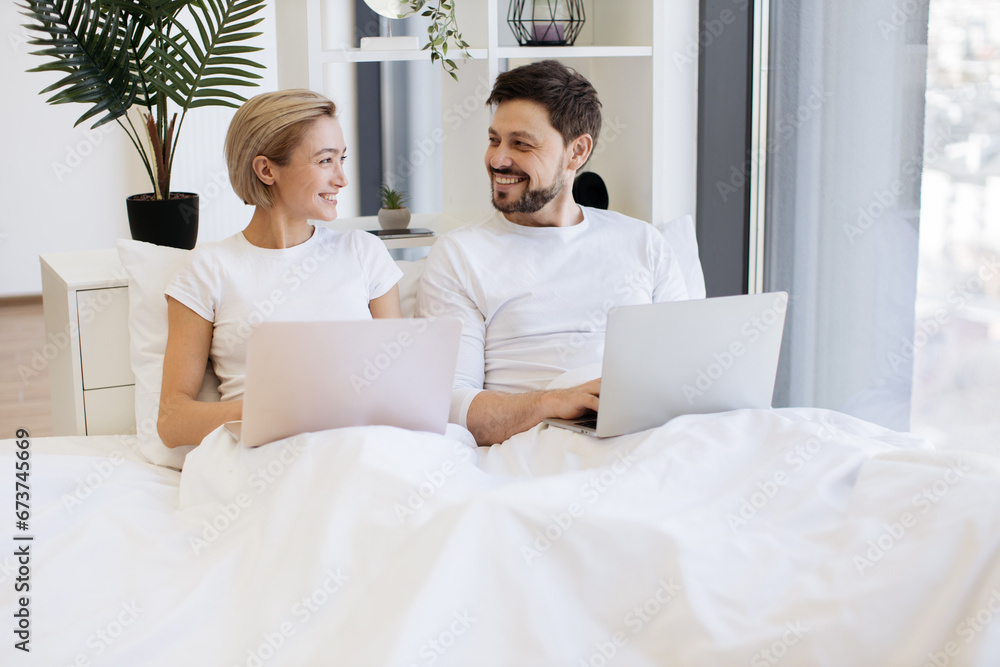 Cheerful amorous people accessing portable computers while spending time together in spacious apartment at weekend. Joyful caucasian family scrolling social media on wireless laptops. Cheerful amorous people accessing portable computers while spending time together in spacious apartment at weekend. Joyful caucasian family scrolling social media on wireless laptops.