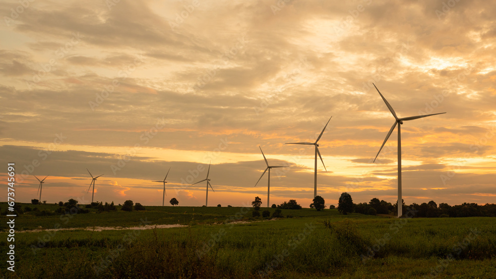 Fototapeta premium Wind turbines generate electricity in a rural area during sunset. Windmill farm on mountain with sunset sky. Wind energy, renewable energy, Green technology.