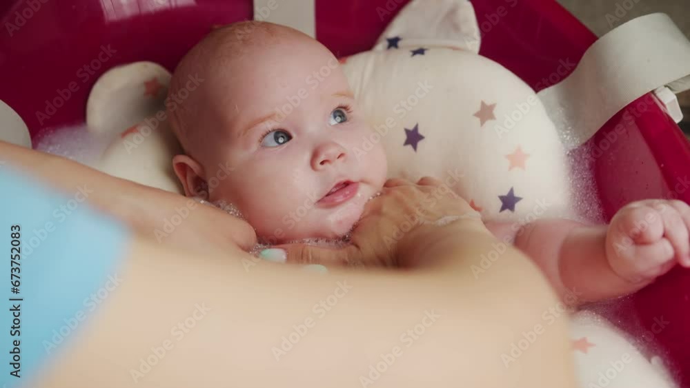Newborn baby taking a bath in a red bathtub with foam Newborn baby taking a bath in a red bathtub with foam