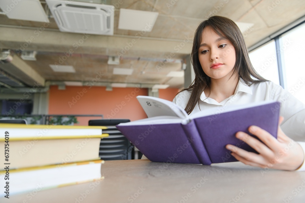 Teen girl studying with textbook writing essay learning in classroom. Teen girl studying with textbook writing essay learning in classroom.
