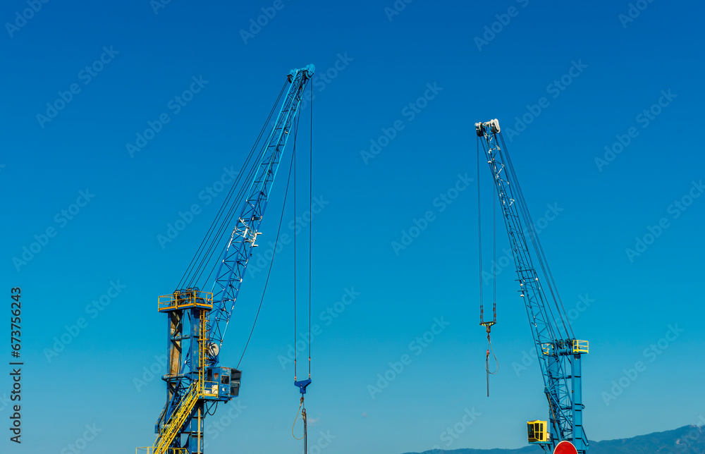 Two construction tower cranes at a construction site against a blue sky with clouds. Two construction tower cranes at a construction site against a blue sky with clouds.