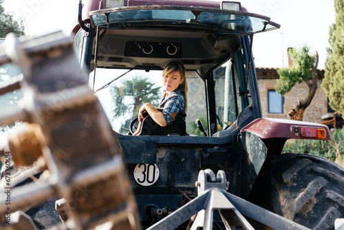 Female farmer driving tractor backwards during summer day