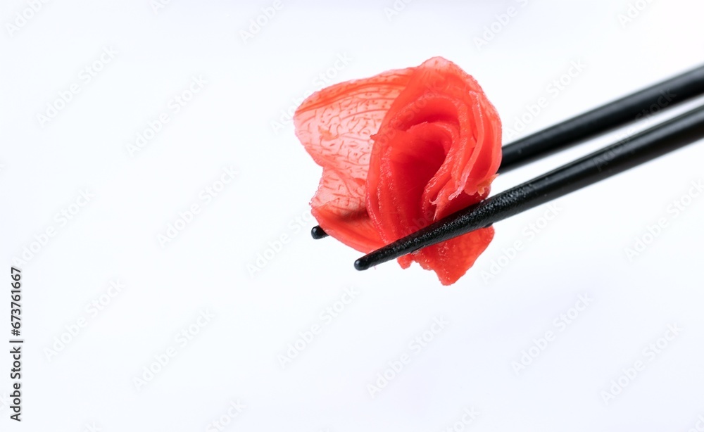 Black japanese chopsticks hold pickled ginger. Spice for sushi, meat, seafood and broth on white background. Fibrous texture. Space for text. Black japanese chopsticks hold pickled ginger. Spice for sushi, meat, seafood and broth on white background. Fibrous texture. Space for text.