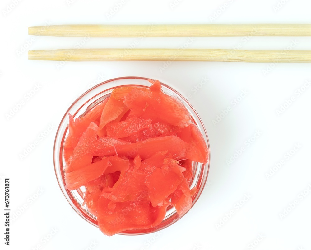 Close-up of transparent dish with marinated ginger and wooden chopsticks. Top view of ingredient for sushi on white surface. Close-up of transparent dish with marinated ginger and wooden chopsticks. Top view of ingredient for sushi on white surface.