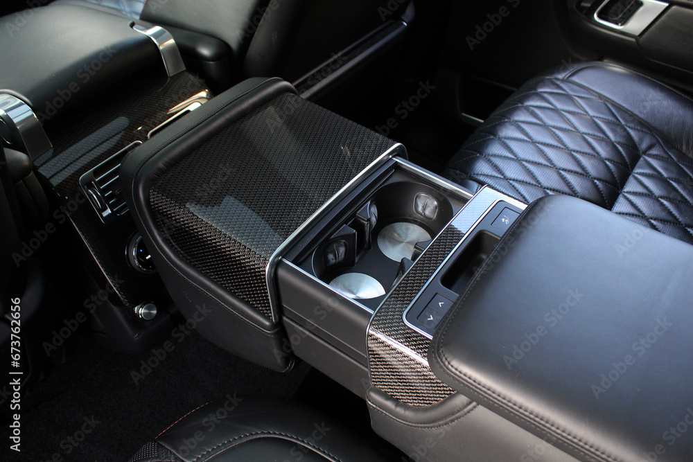 Armrest with table and cup holder in luxury SUV. Black Leather folding armrest with cup holders in rear seats inside a vehicle. Armrest with table and cup holder in luxury SUV. Black Leather folding armrest with cup holders in rear seats inside a vehicle.