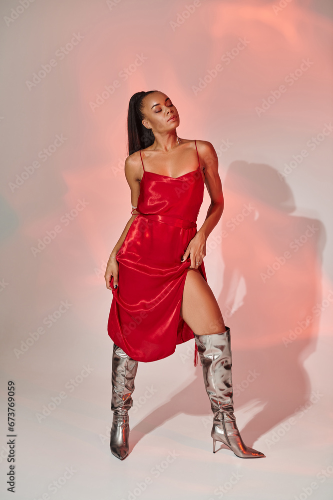 full length, african american woman in red midi dress and silver boots posing on grey with lighting full length, african american woman in red midi dress and silver boots posing on grey with lighting