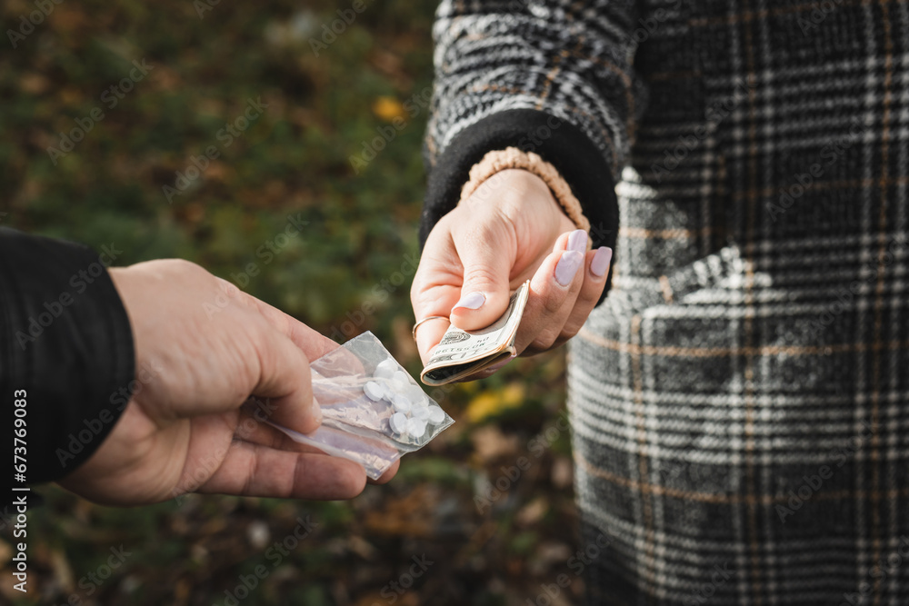 Male drug dealer sells hard drugs in a transparent plastic bag to an addicted woman with money in her hand, cropped image - obrazy, fototapety, plakaty 