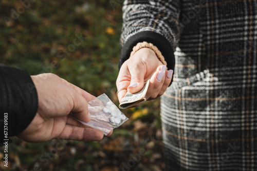Male drug dealer sells hard drugs in a transparent plastic bag to an addicted woman with money in her hand, cropped image