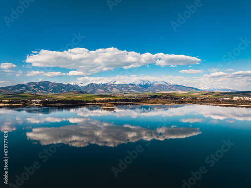 Aerial view from above the water surface of Liptovska Mara water reservoir on serene nature landscape, the High Tatras Mountains in the distance. © Halfpoint
