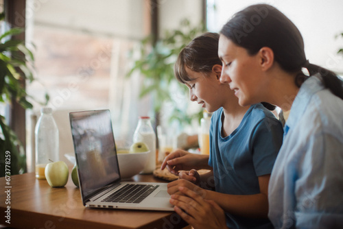 Mom and daughter watching entertaining videos on mom's work laptop. Remote work, home office for mothers with children.