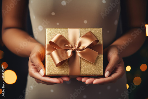 a woman hand holding a luxury gift box with bow against a christmas background, Woman holding beautiful gift box against blurred festive lights, closeup © Planetz