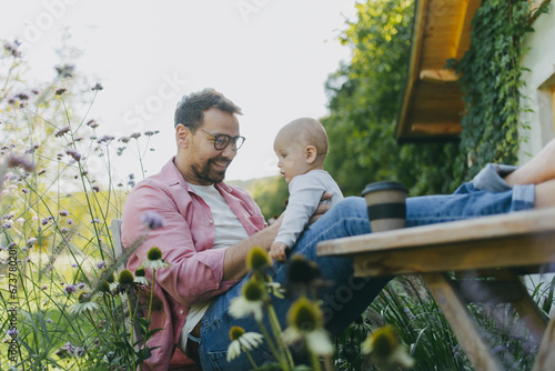 Man sitting in the garden with feet on table, playing with his baby son. Father having bonding moment with his little kid.