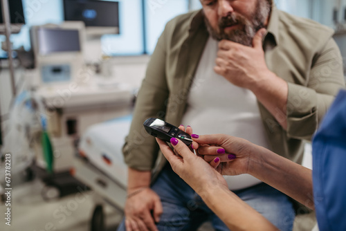 Doctor checking blood glucose level using a fingerstick glucose meter, waiting for results from glucometer. Obese, overweight man is at risk of developing type 2 diabetes. Concept of health risks of
