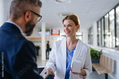 Pharmaceutical sales representative shaking hand with female doctor in medical building. Hospital director consulting with healthcare staff. photo