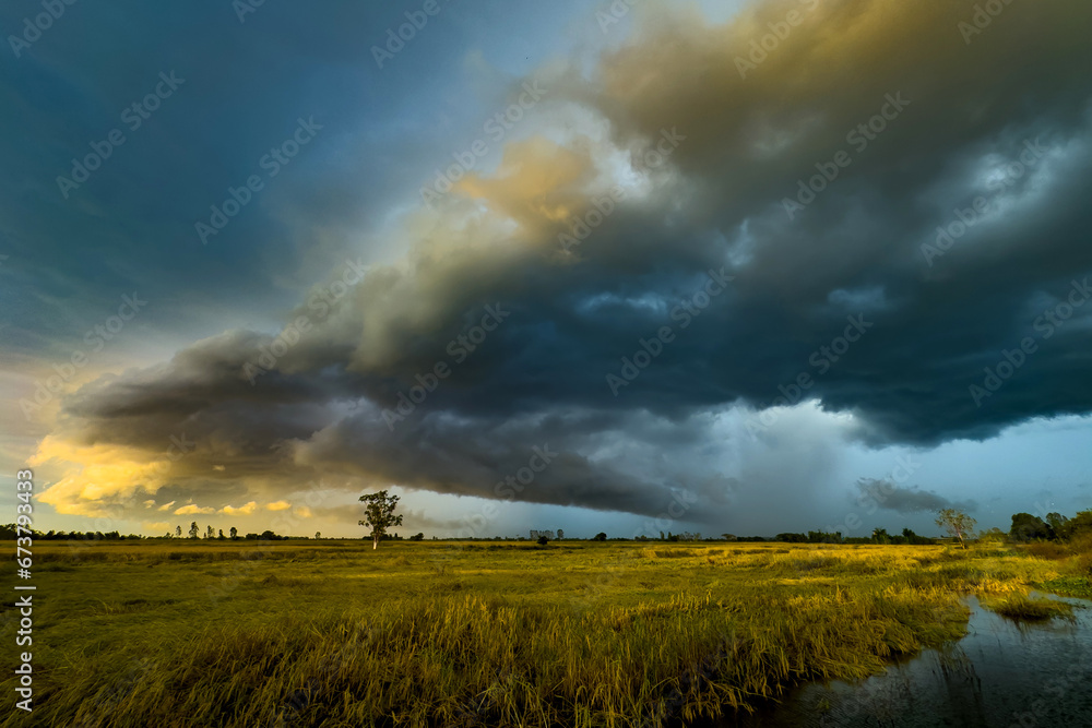 Fototapeta premium Photo of Super storm with sun light , Dark sunset sky and dramatic black cloud before rain.rainy storm over rice fields,countryside Thailand,ASIA.