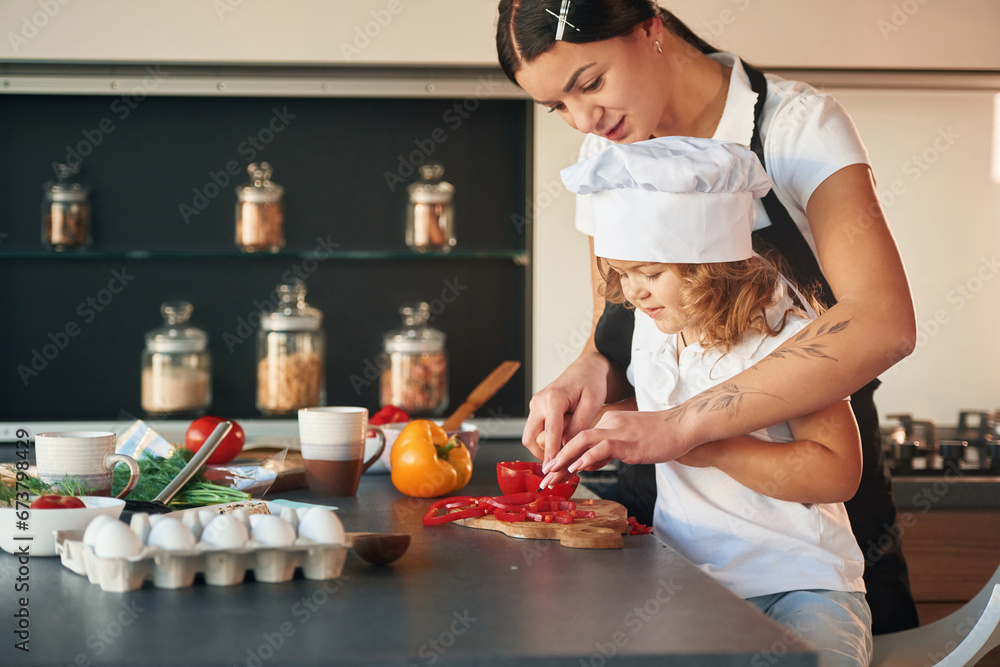 Side view. Mother with her daughter are preparing food on the kitchen Side view. Mother with her daughter are preparing food on the kitchen