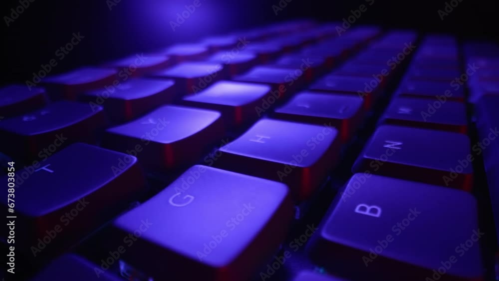 Super macro dolly of computer keyboard buttons in neon light. Working at night, online video games, e-sports. Cyberspace concept