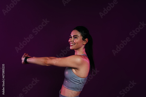 Young smiling woman stretching and flexing her hands over magenta background in studio
