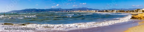 High-resolution panorama of the coast of Palma de Mallorca waves with foam in the foreground run up the shore in the distance hotels are visible against the background of the Tramuntana mountains