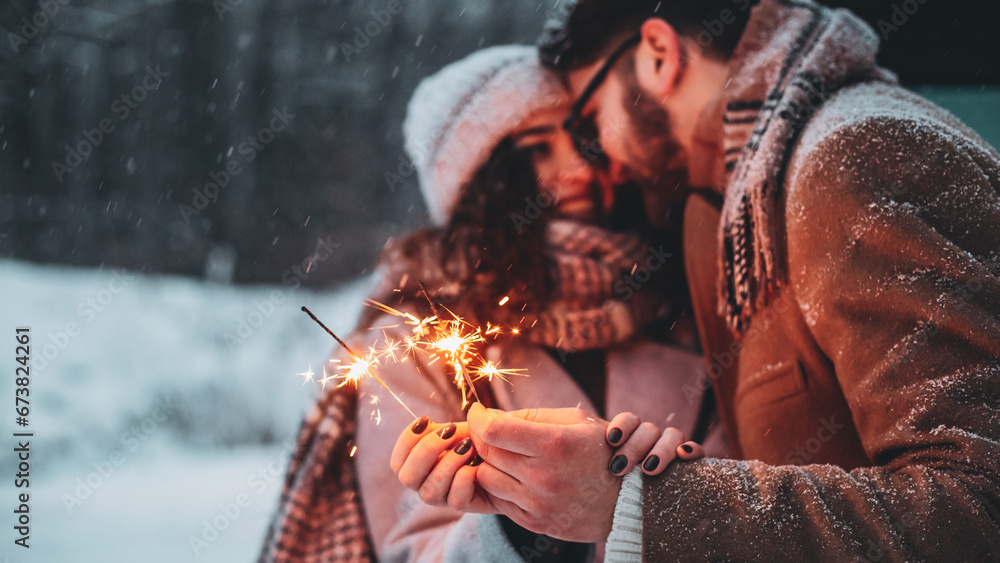 Outdoor waist up portrait of young beautiful happy smiling couple posing on street. Models hugging, looking at each other, holding sparkles, wearing stylish clothes. Snowfall. Copy, empty space - obrazy, fototapety, plakaty 