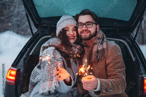 Romantic couple in love celebrate together the new year with fire sparkler at the back of car. Love is in the air. Christmas time.