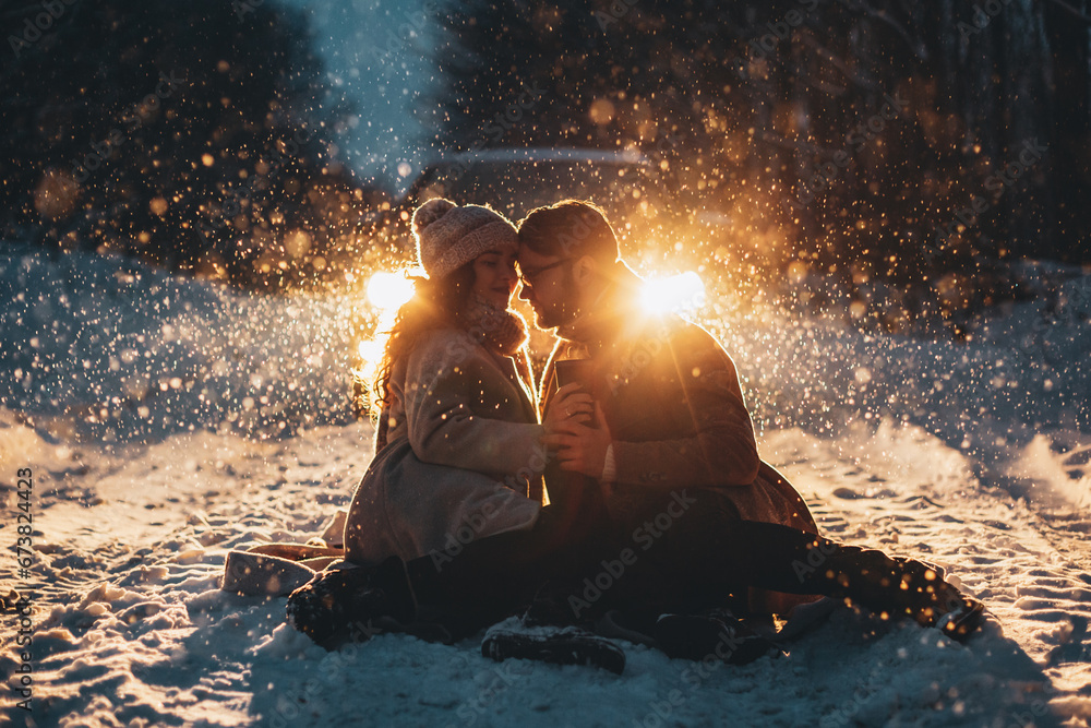 Happy couple playful together during winter holidays vacation outside in snow park at night time with car`s ligths on background. - obrazy, fototapety, plakaty 