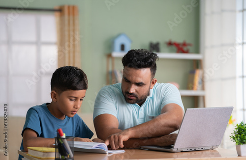 Indian father helping his son for reading while working on laptop at home - concept of Educational assistance, Parental guidance and Multitasking