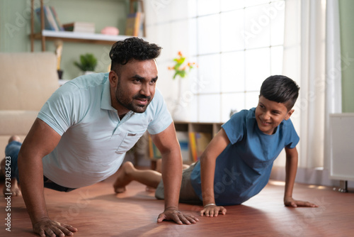 Joyful indian father with son doing push ups exercise at home - concept of Joyful fitness  Active lifestyle and healthy habits