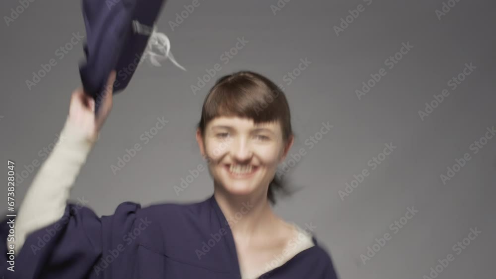 Graduation girl holding cap in hands. Female student jumping and smiling against gray background. Graduation girl holding cap in hands. Female student jumping and smiling against gray background.
