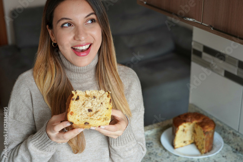 Beautiful young woman eating a slice of Panettone on Christmas holiday looking to the side thinking indoor. Copy space.