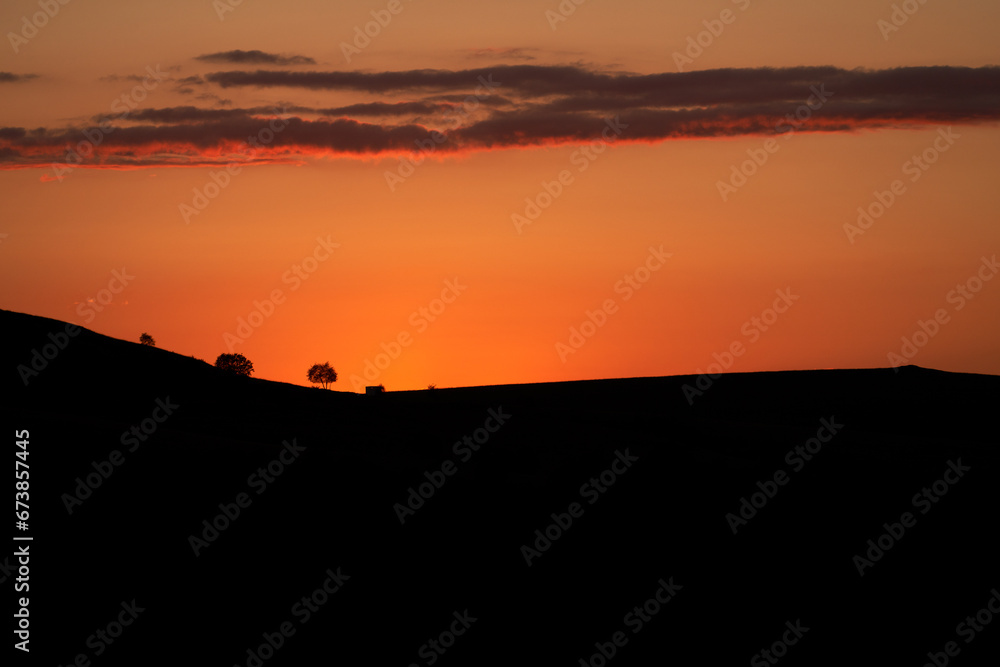 Sunset. The sun has dropped behind the mountains. Outline of mountainous terrain with solitary trees under red sky. Copy space.