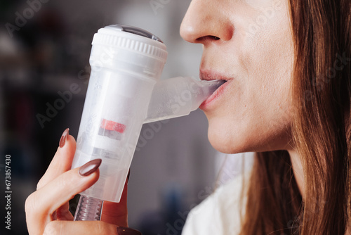 Nebulizer device in mouth. Woman with inhaler in her mouth background. Breathing saline through nebulization. Mouth inserted nebulizer. Lung and throat treatment.