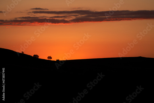 Sunset. The sun has dropped behind the mountains. Outline of mountainous terrain with solitary trees under red sky. Copy space.