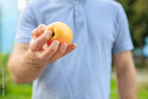 Man's hand holds an apple, snack and fast food concept. Selective focus on hands with blurred background