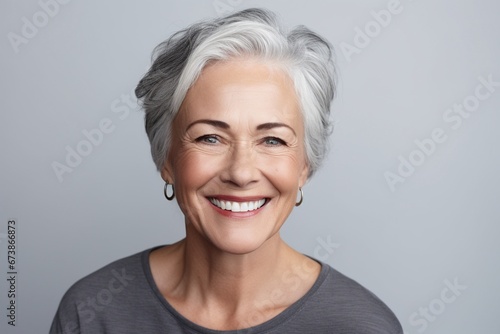 Graceful Aging: A Smiling and Happy Mature Lady Graces a Plain Grey Background, Exuding Contentment, Cheerfulness, and the Inner Peace of Retirement