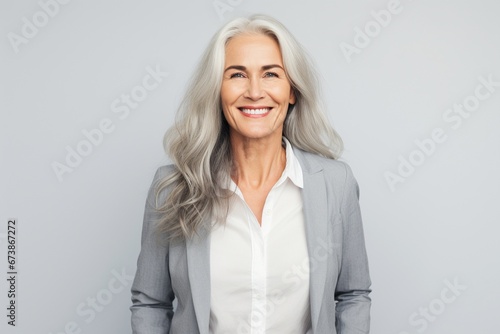 Graceful Aging: A Smiling and Happy Mature Lady Graces a Plain Grey Background, Exuding Contentment, Cheerfulness, and the Inner Peace of Retirement