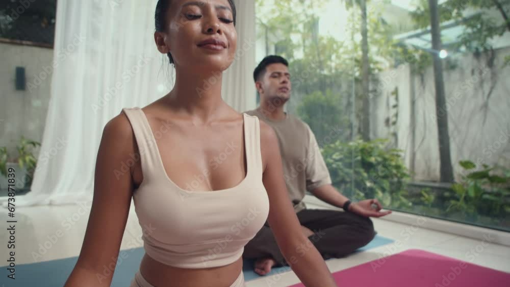 Tilt up shot of multicultural couple meditating on mat with eyes closed while sitting in lotus position at home Tilt up shot of multicultural couple meditating on mat with eyes closed while sitting in lotus position at home