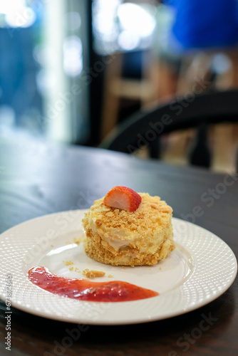 Napoleon cake  made with layers of puff with whipped cream and crumbs with Strawberry on top and sauce served on plate