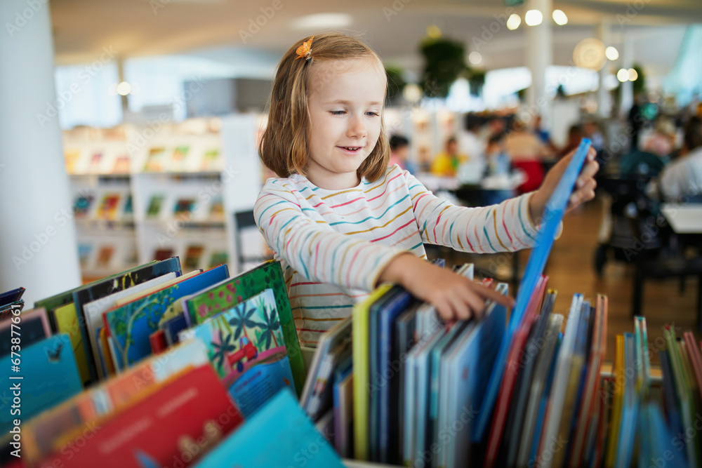 Five year old girl selecting a book in municipal library - obrazy, fototapety, plakaty 