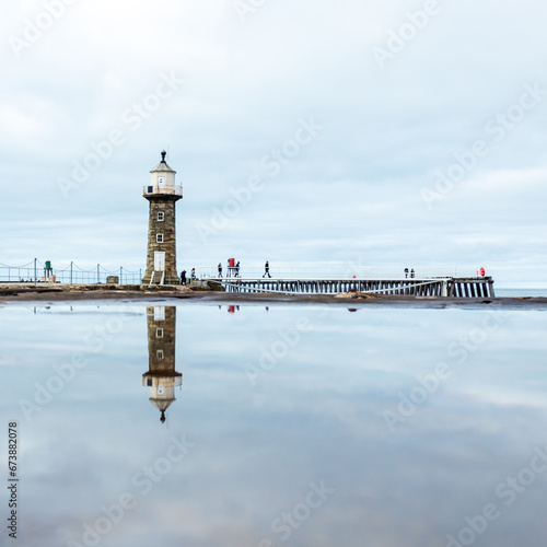 Whitby Pier and Lighthouse with full reflection in puddle