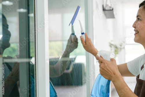 Woman cleaning glass with wiper and spray.