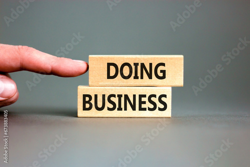 Doing business symbol. Concept words Doing business on beautiful wooden block. Beautiful grey table grey background. Businessman hand. Business, motivational Doing business concept. Copy space.